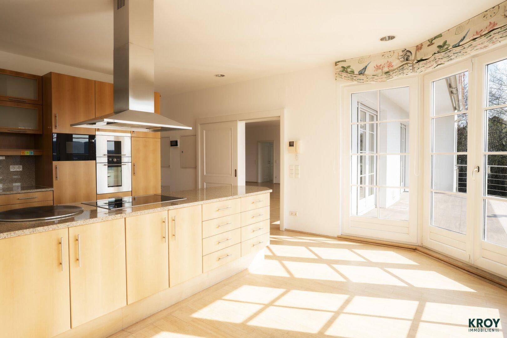 Moderne Küche mit hellen Holzfronten, Granitarbeitsplatte und viel Tageslicht durch große Fenster.