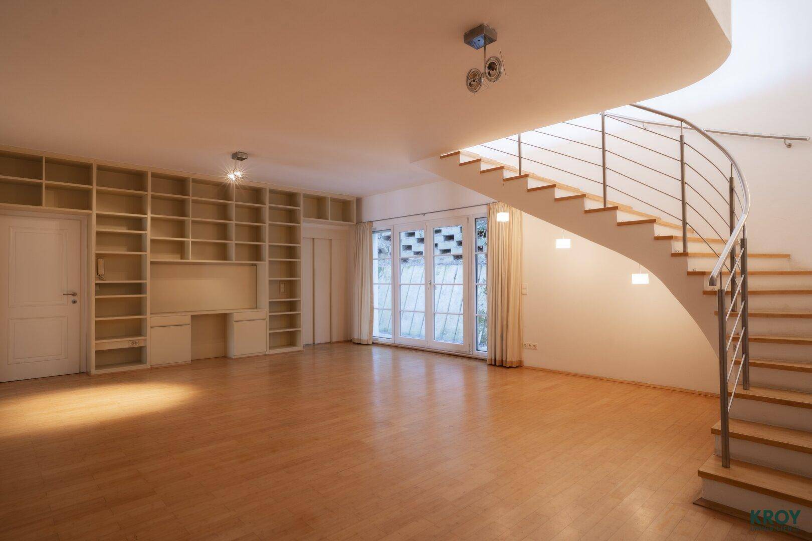 Heller Wohnbereich mit Holzboden, Einbauregalen und einer eleganten geschwungenen Treppe.