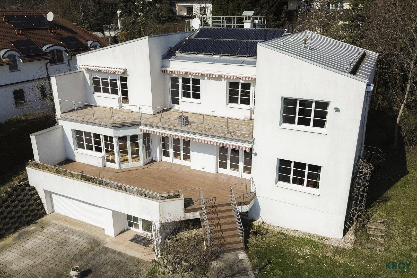 Luftaufnahme des modernen weißen Gebäudes mit mehreren Terrassen und Solarpaneelen auf dem Dach.