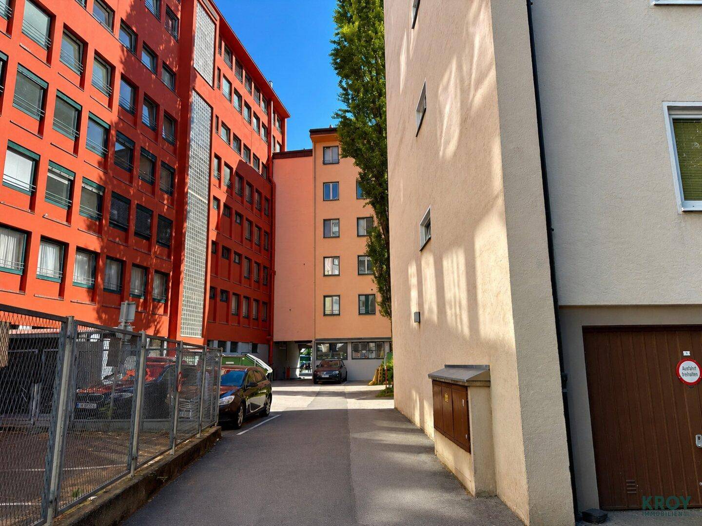 Ansicht von Gebäuden mit unterschiedlichen Fassadenfarben und einem Durchgang mit geparkten Autos.