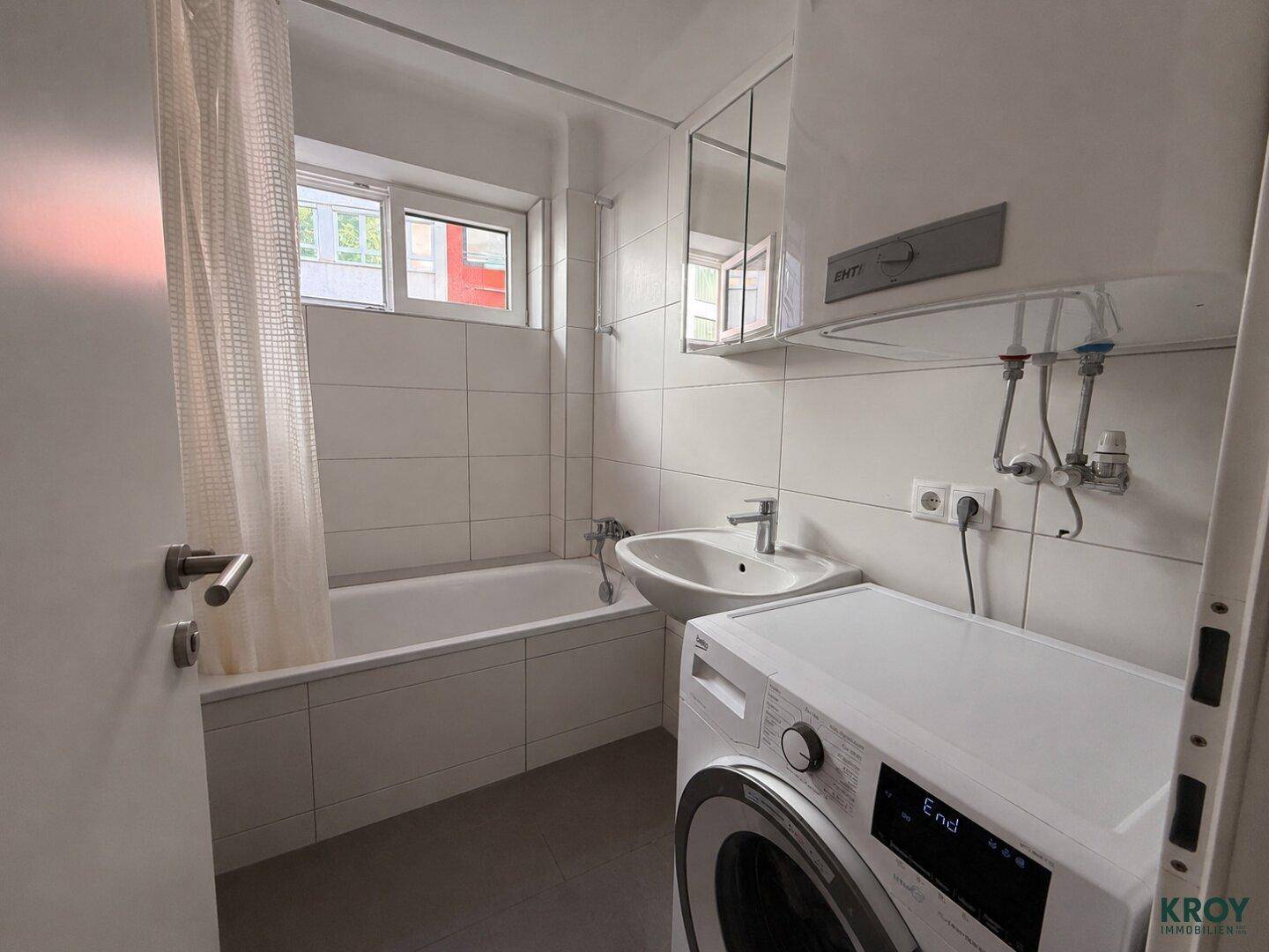 Badezimmer mit Badewanne, Waschbecken, Waschmaschine und Fenster.