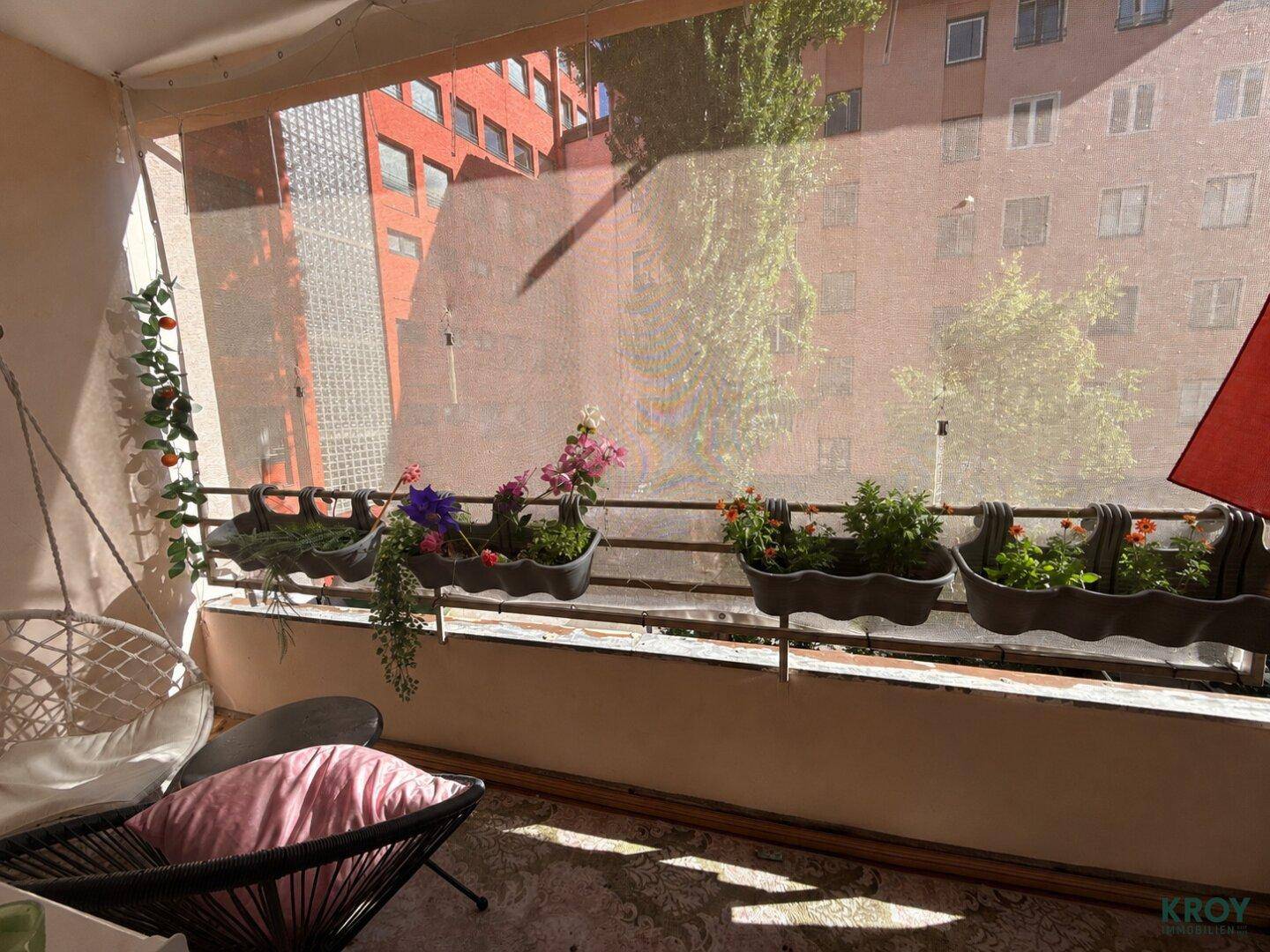 Gemütlicher Balkon mit Blumenkästen, Hängesessel und Blick auf umliegende Gebäude.