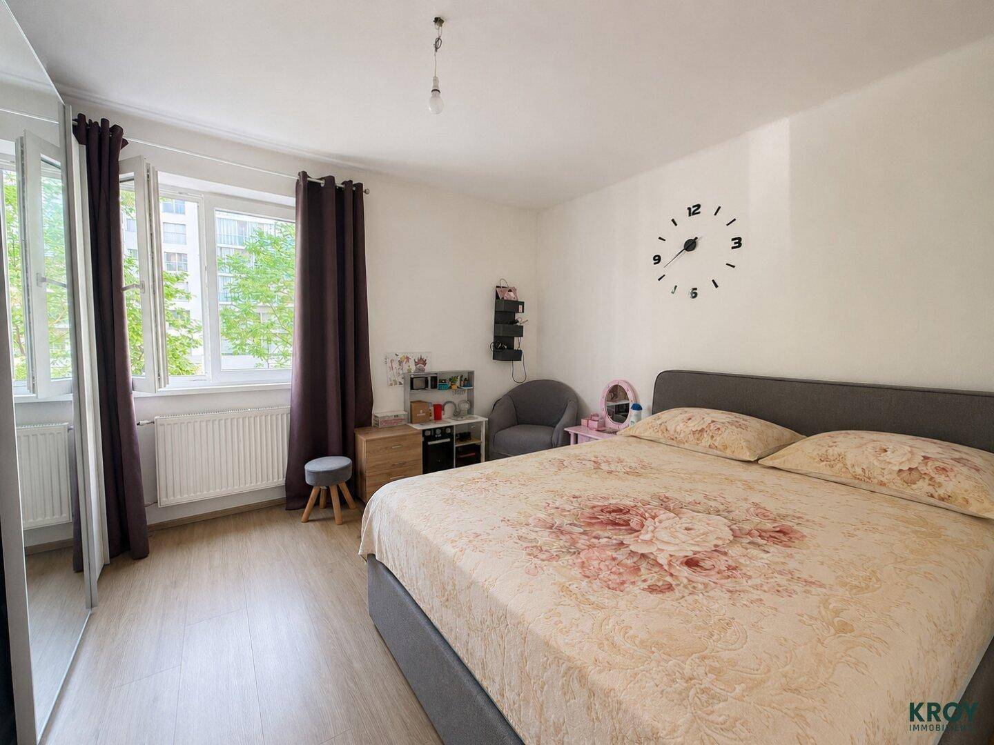 Helles Schlafzimmer mit großem Fenster, Vorhängen und Kleiderschrank.
