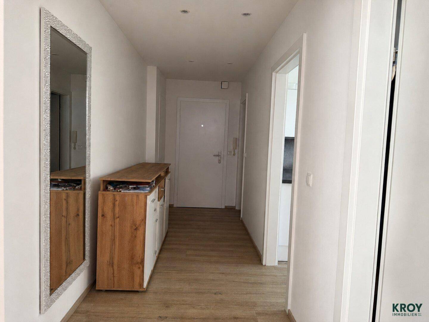 Heller Flur mit großem Spiegel, Holzkommode und Laminatboden.