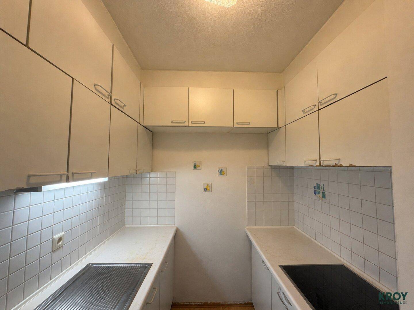 Schmale Küche mit weißen Einbauschränken, Fliesenrückwand und Spülbecken.