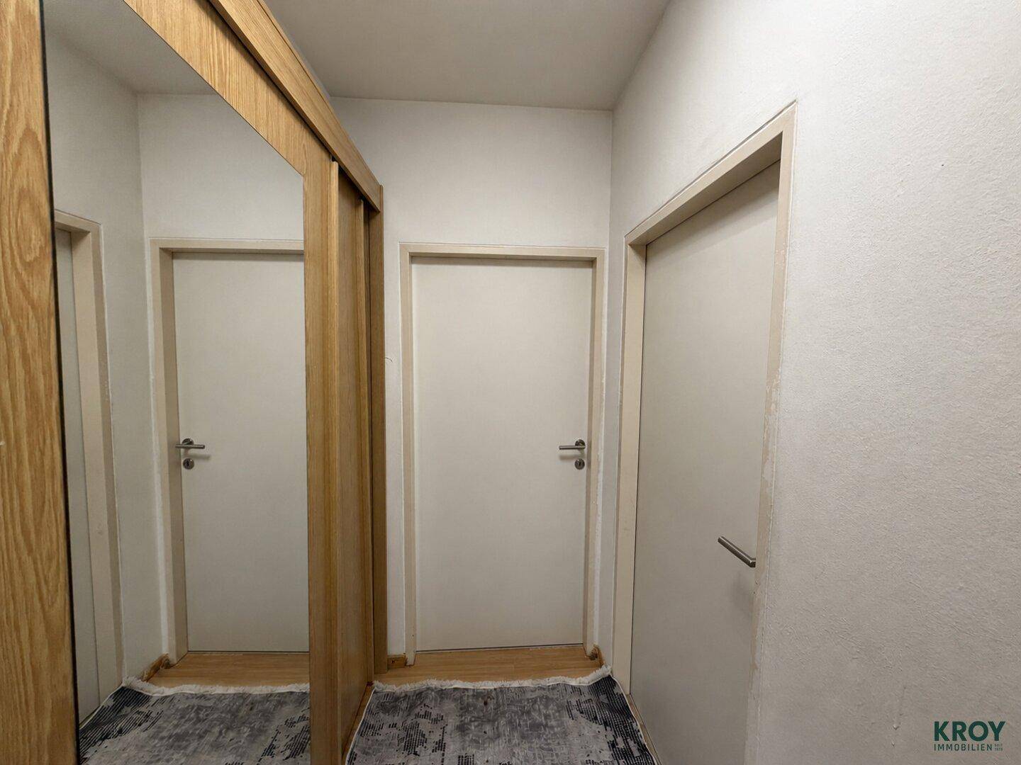 Heller Flur mit Spiegelschiebetüren und mehreren Zimmertüren.