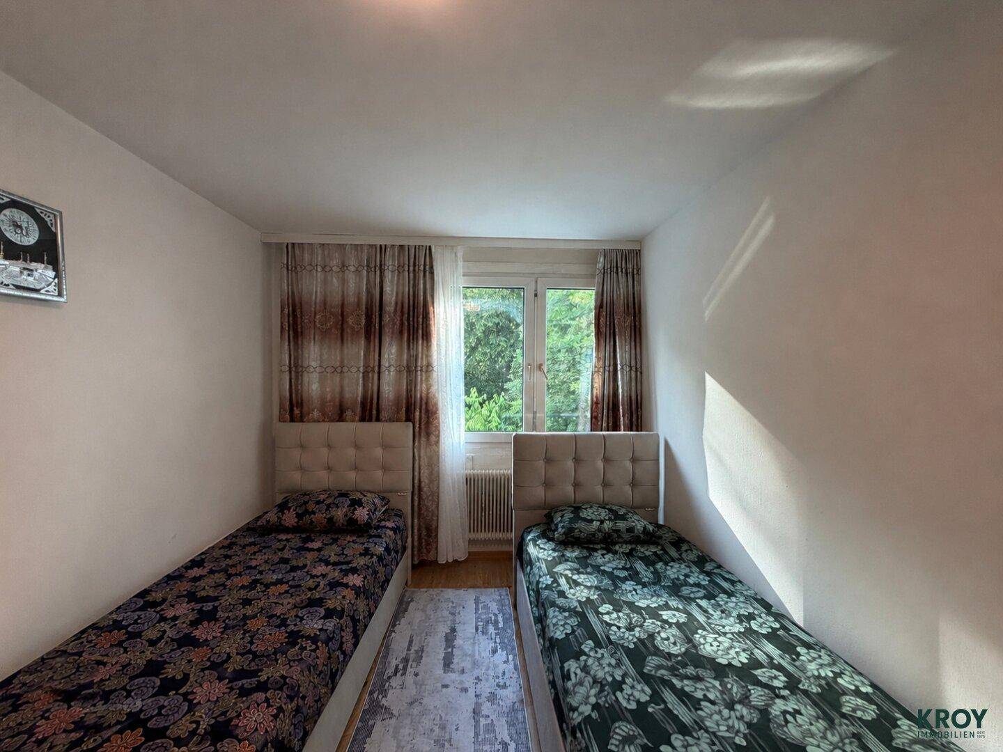 Schlafzimmer mit zwei Einzelbetten, Fenster und Blick auf Bäume.