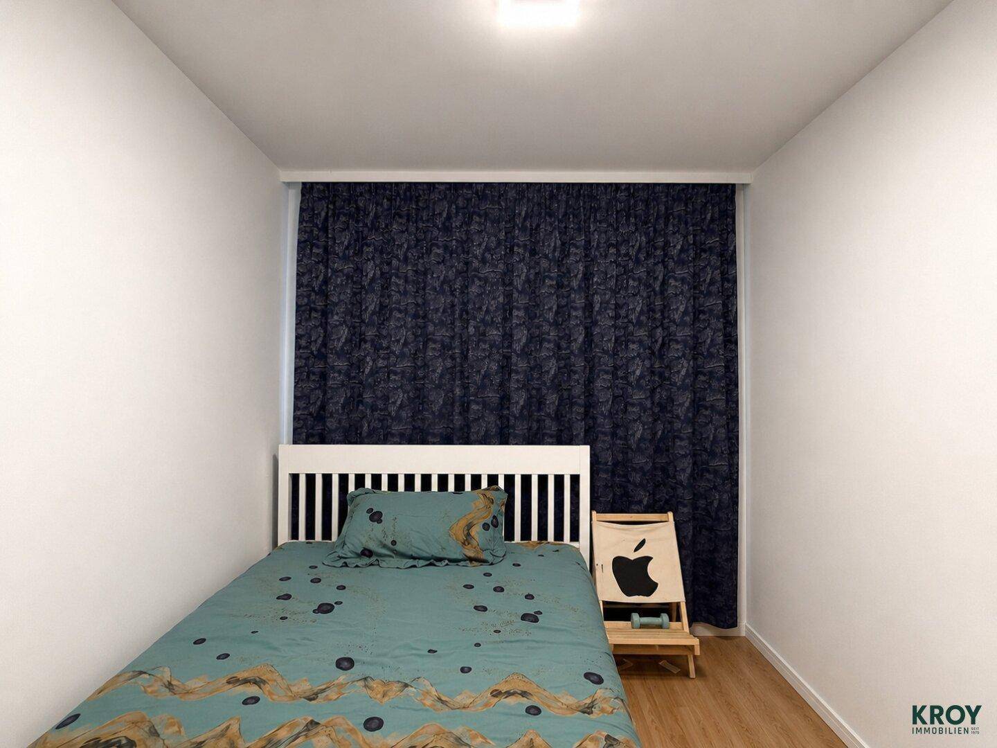 Kleines Schlafzimmer mit Einzelbett, dunklen Vorhängen und Holzfußboden.