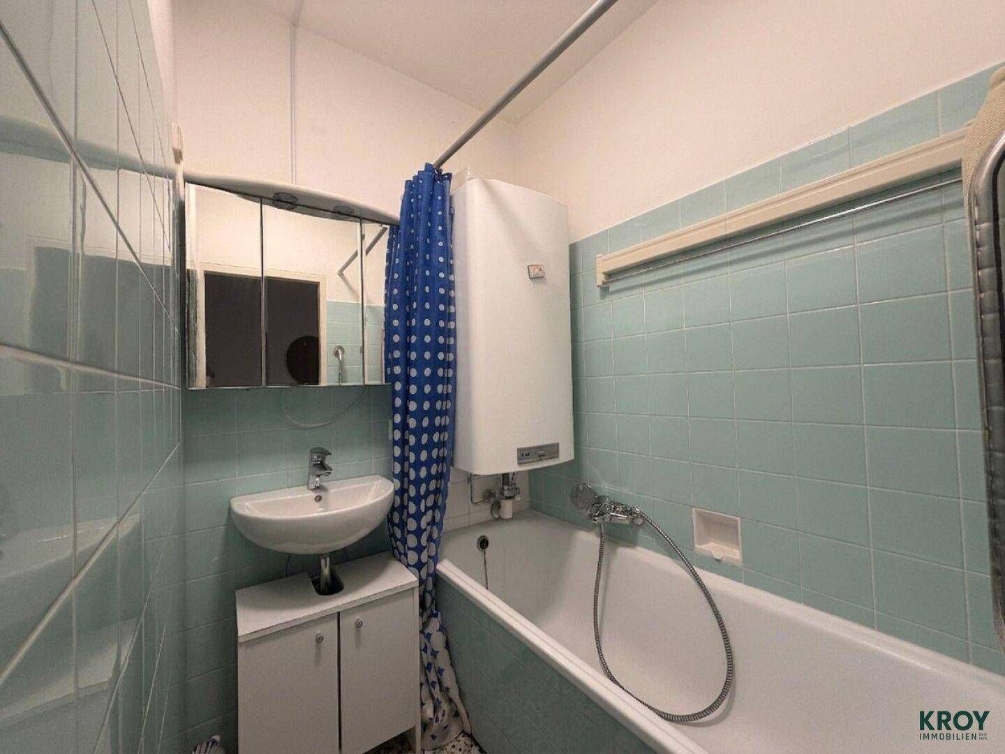 Badezimmer mit hellblauen Fliesen, Badewanne, Waschbecken und Spiegelschrank.