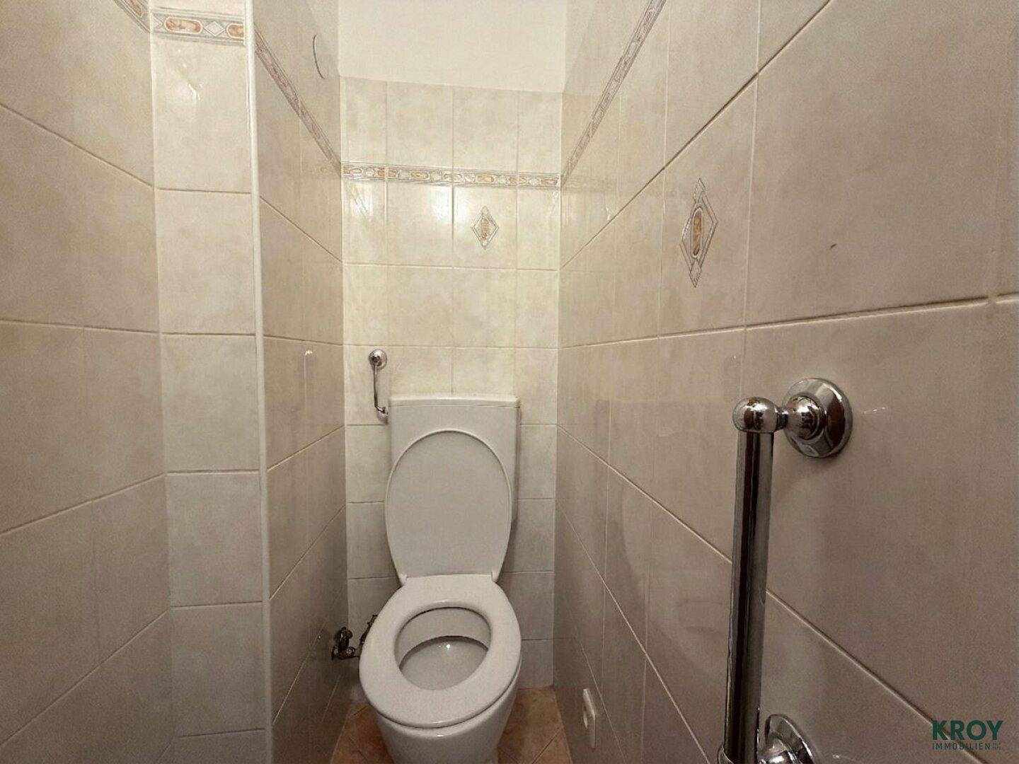 Separate Toilette mit beigefarbenen Fliesen und Wand-WC.