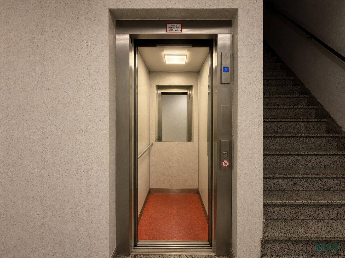 Moderner Aufzug mit Edelstahltüren und rotem Teppich im Eingangsbereich.