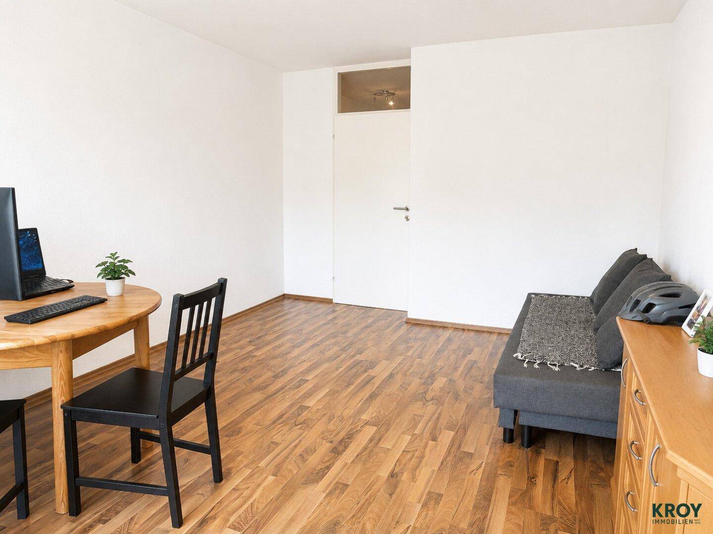 Geräumiges Wohnzimmer mit Laminatboden, Sofa und Schreibtischbereich, hell und funktional eingerichtet.