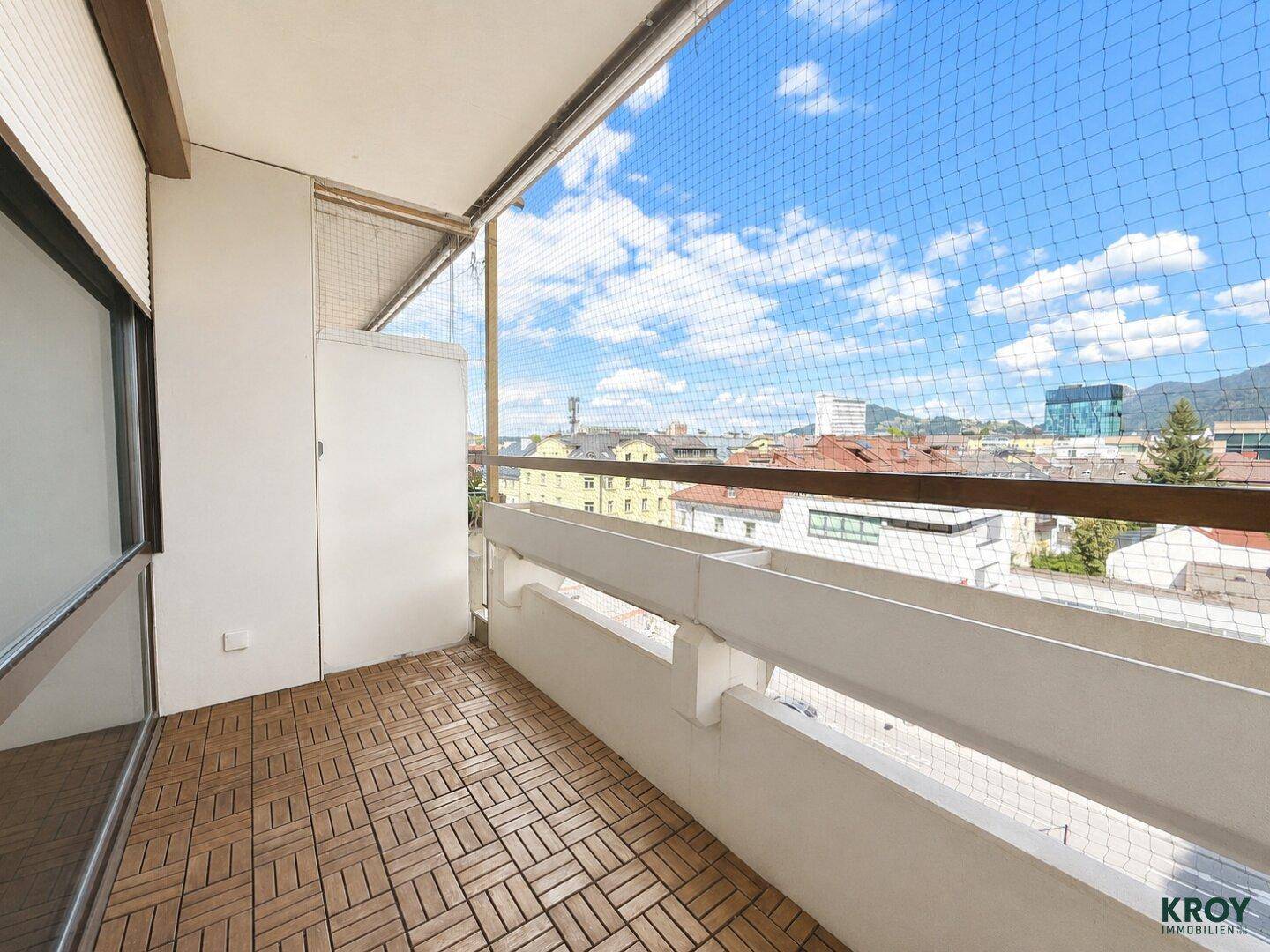 Heller Balkon mit Holzbodenfliesen und weitem Blick über die Stadt und Berge.