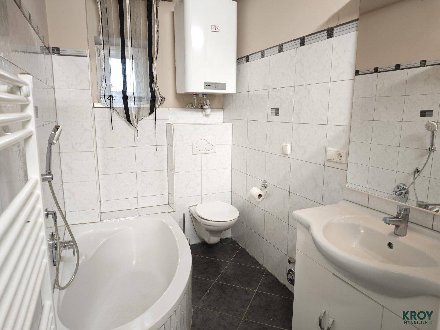 Gefliestes Badezimmer mit Eckbadewanne, WC, Waschbecken und Heizkörper.