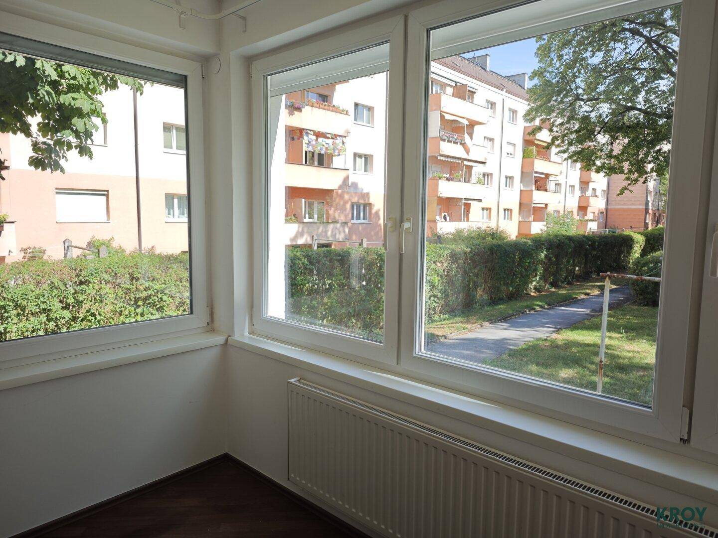 Eckfenster bieten einen weiten Blick auf die gepflegte Wohnanlage und Bäume.