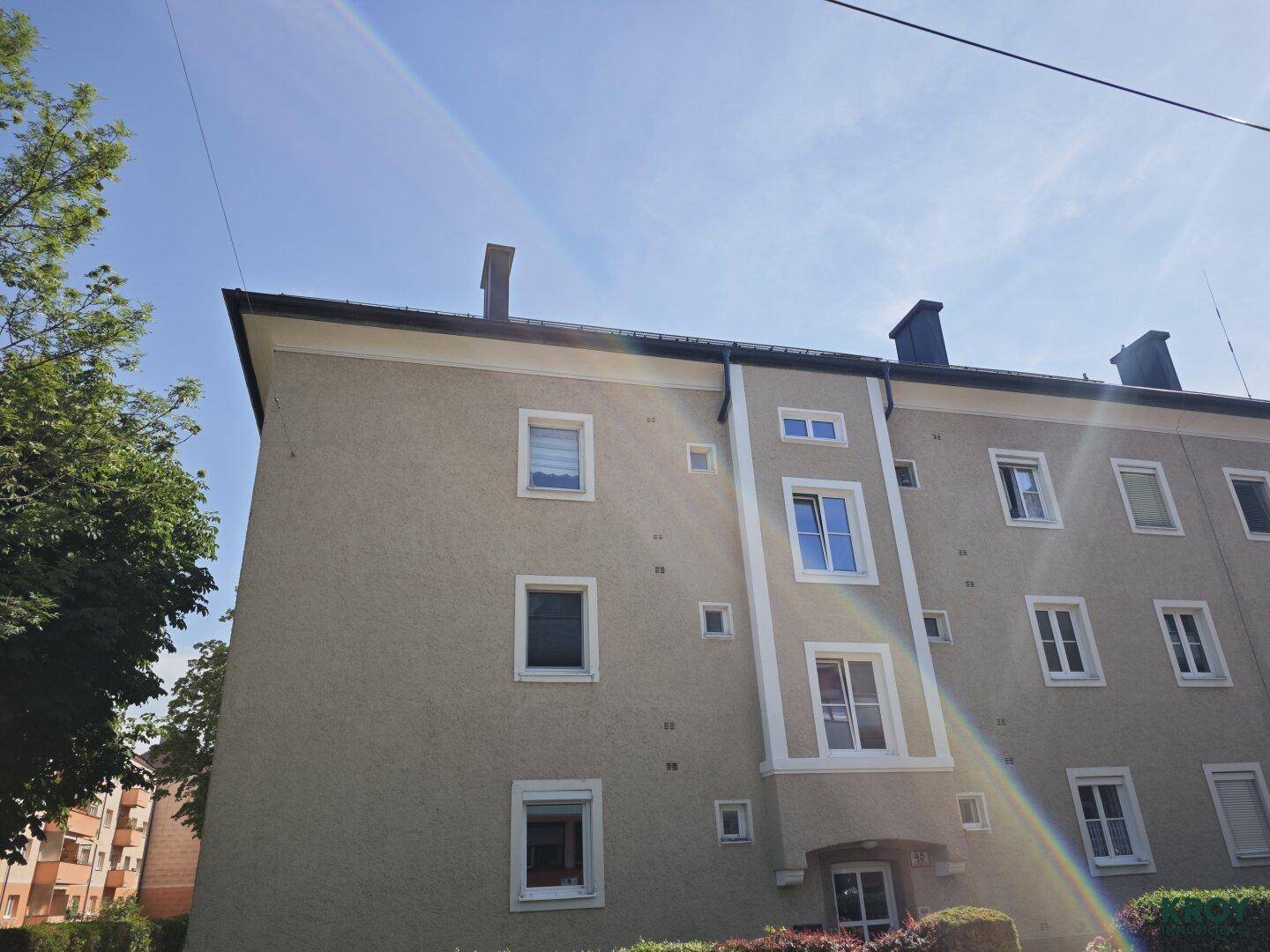 Außenansicht des Wohngebäudes unter blauem Himmel mit Bäumen im Hintergrund.