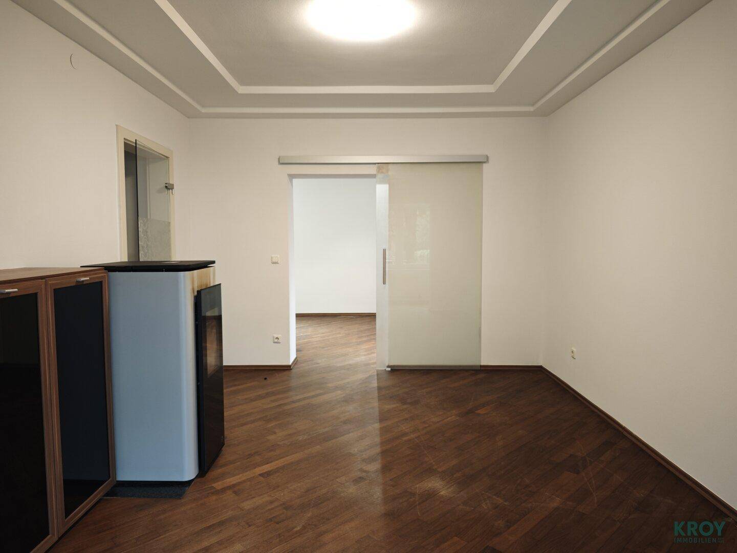 Geräumiges Wohnzimmer mit Holzboden und moderner Glasschiebetür zu einem weiteren Raum.