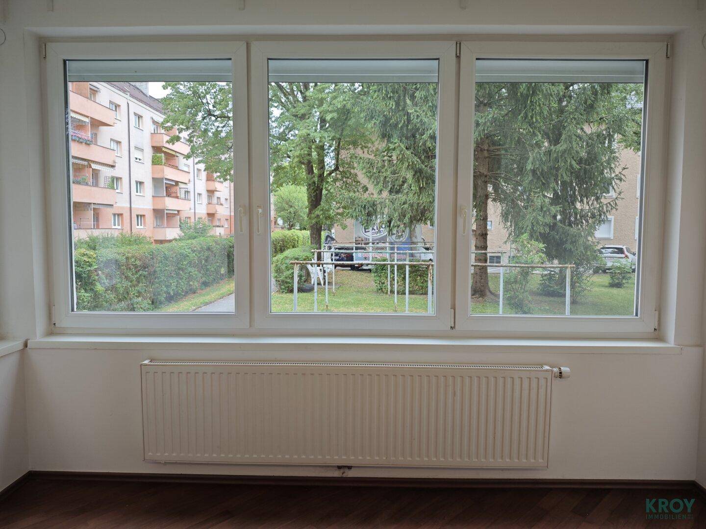 Große Fensterfront mit Blick auf die grüne Umgebung und gegenüberliegende Gebäude.