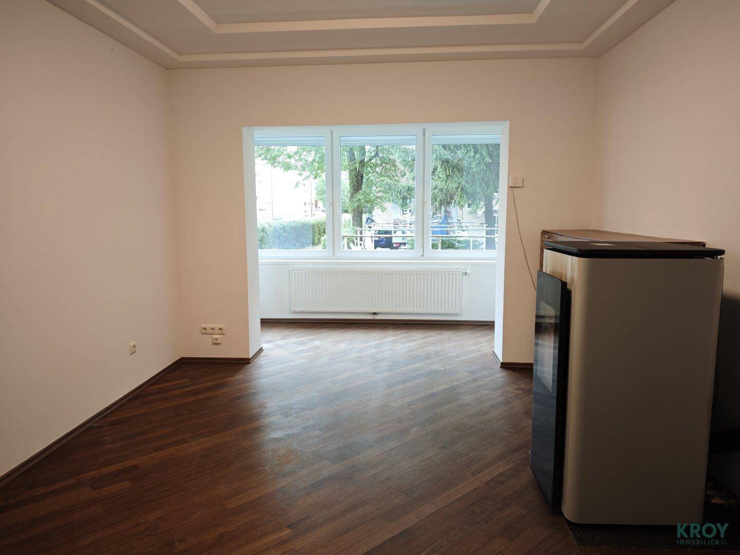 Helles Wohnzimmer mit dunklem Parkettboden, großen Fenstern und Blick ins Grüne.