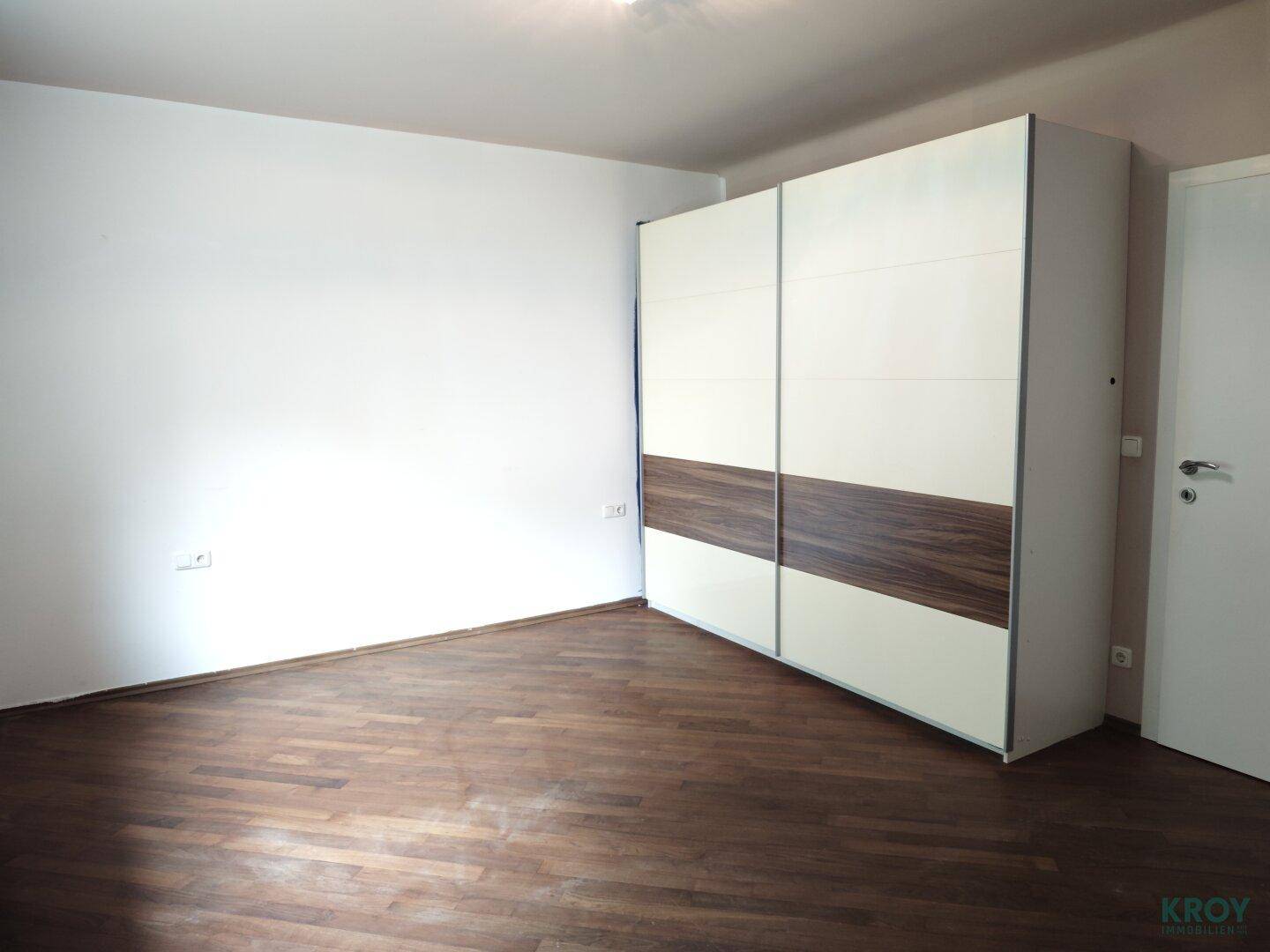 Schlafzimmer mit modernem Schiebetürenschrank und dunklem Parkettboden.