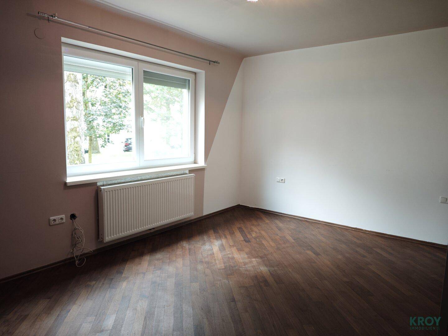Geräumiges Schlafzimmer mit Holzboden und großem Fenster, das viel Tageslicht hereinlässt.
