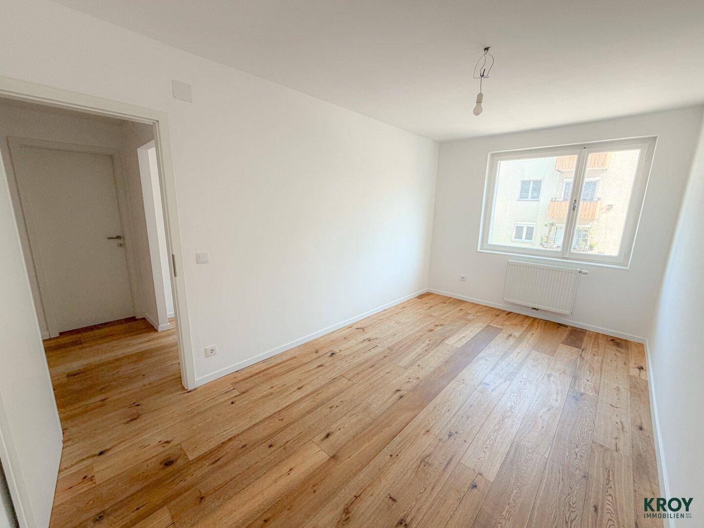 Geräumiges Schlafzimmer mit Holzboden und großem Fenster, bietet viel Platz und Tageslicht.