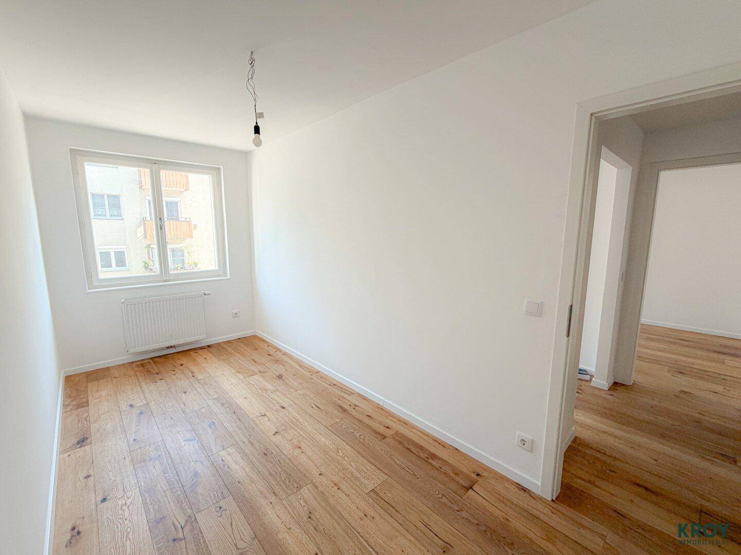 Freundliches Schlafzimmer mit Holzboden und weiß gestrichenen Wänden, bereit zur individuellen Gestaltung.