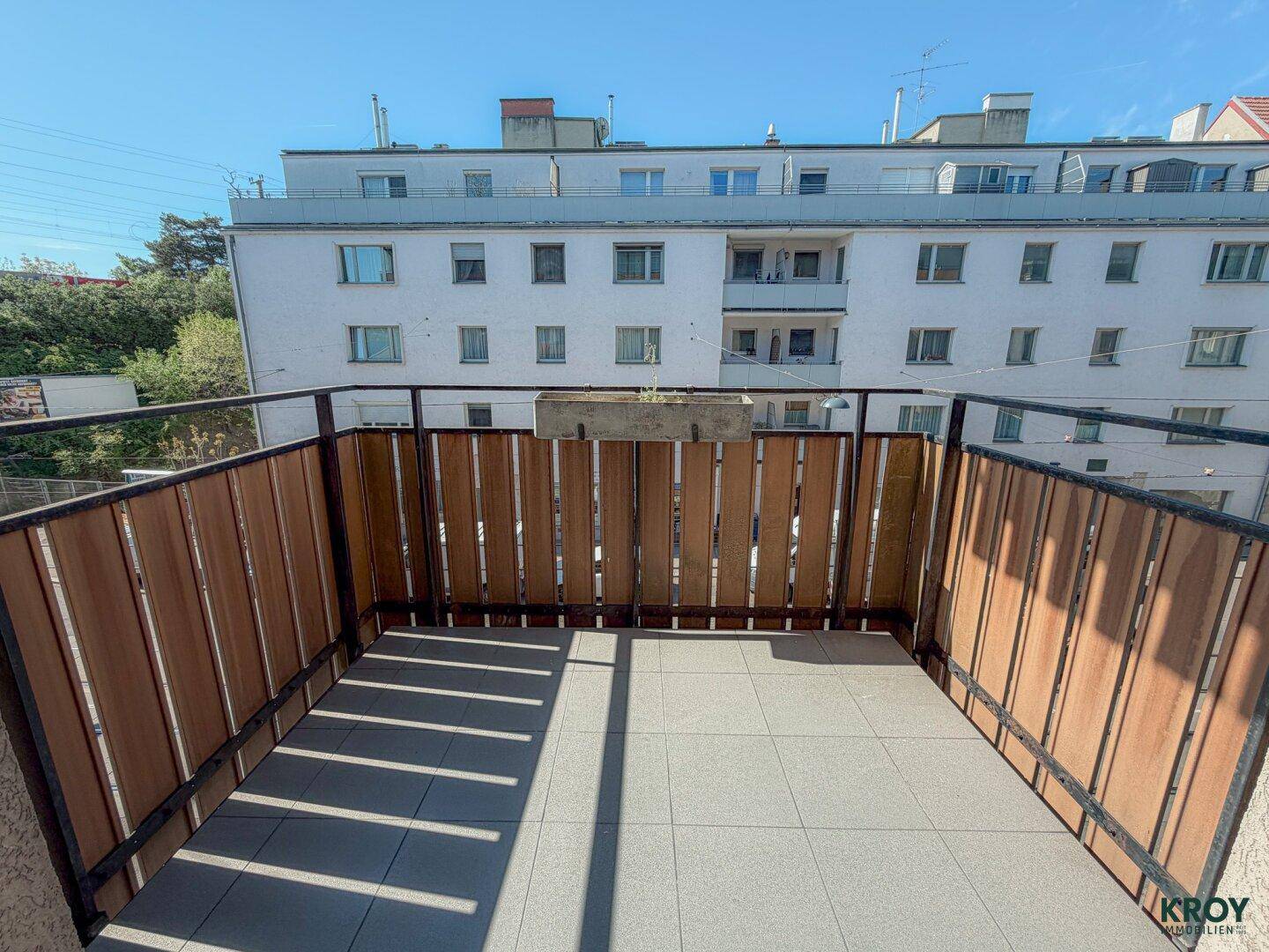 Heller Balkon mit Fliesenboden und Holzverkleidung, bietet einen Blick auf die umliegenden Gebäude.