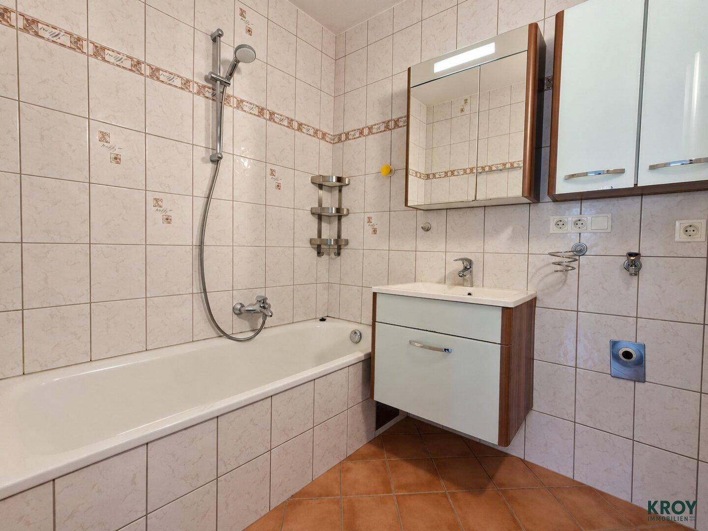 Gefliestes Badezimmer mit Badewanne, integrierter Dusche und einem Waschbecken mit Spiegelschrank.