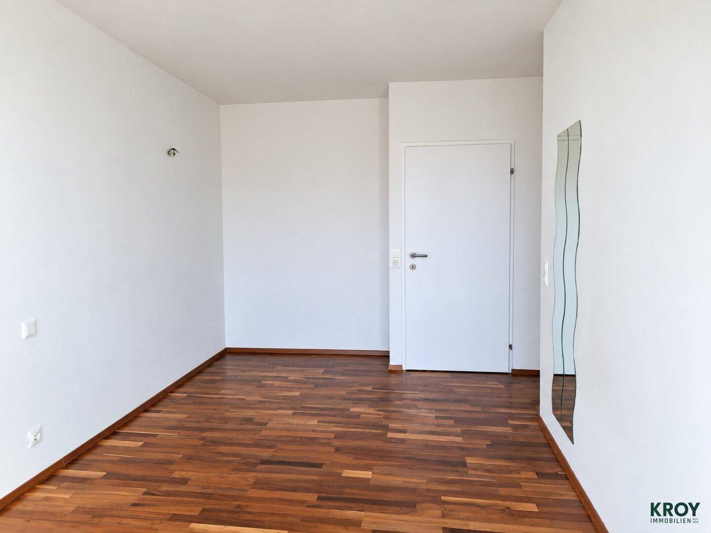 Leeres Schlafzimmer mit warmem Parkettboden und einer weißen Tür, bereit zur Einrichtung.