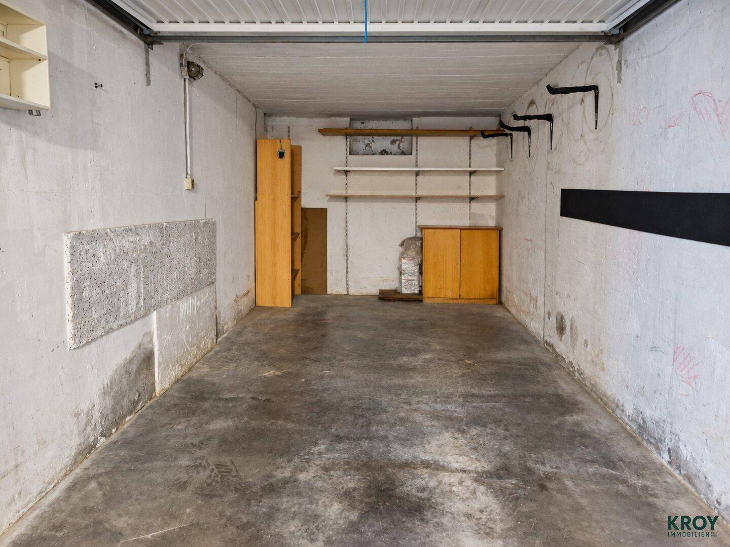 Private Garagenbox mit Betonboden und Regalen für zusätzlichen Stauraum.