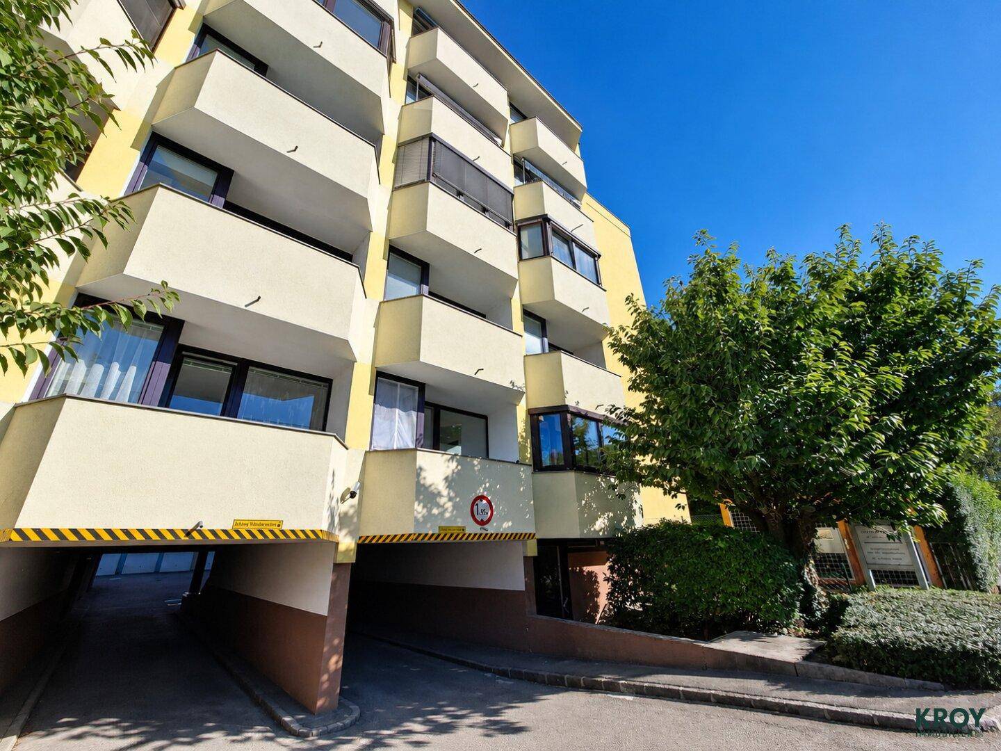 Eingangsbereich eines modernen Wohngebäudes mit Tiefgaragenzufahrt und gepflegter Außenanlage.
