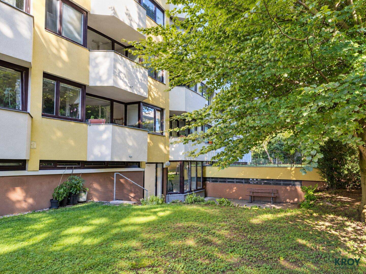 Ruhiger Gartenbereich mit Rasen, Bäumen und einer Holzbank zum Entspannen im Freien.