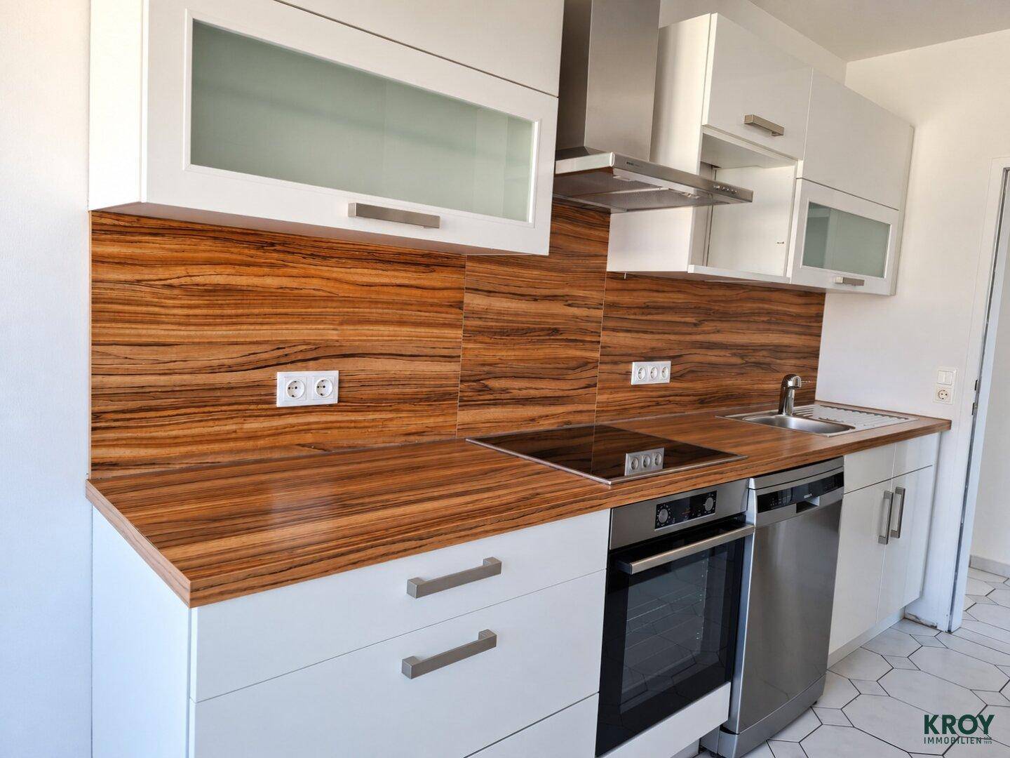 Moderne Einbauküche mit weißen Schränken, Holzoptik-Arbeitsplatten und integrierten Geräten.