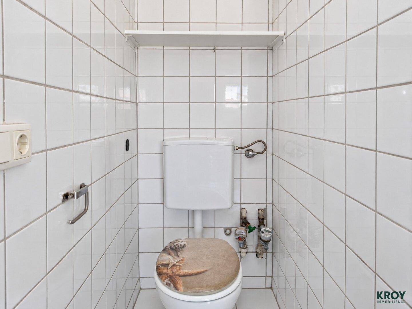 Separates WC mit weißen Fliesen und einer einfachen Toilette, funktional und sauber.