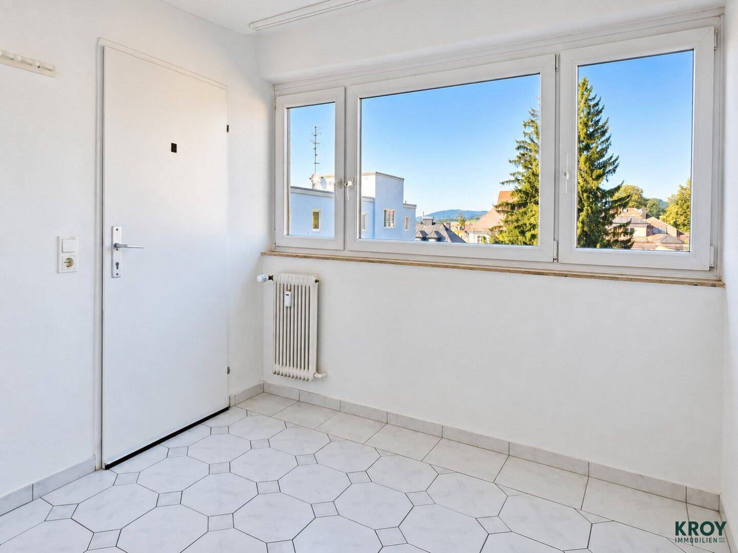 Heller Raum mit Fliesenboden und großen Fenstern, ideal als Büro oder Gästezimmer nutzbar.