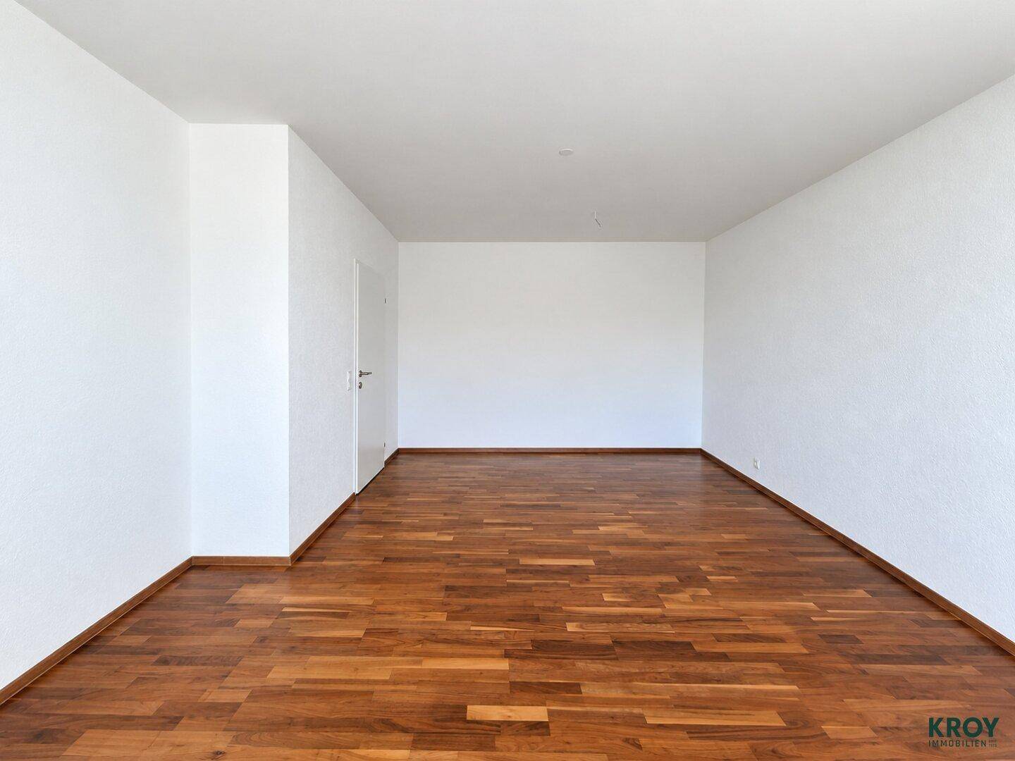 Leeres Zimmer mit warmem Holzparkett und weißen Wänden, bereit zur individuellen Gestaltung.