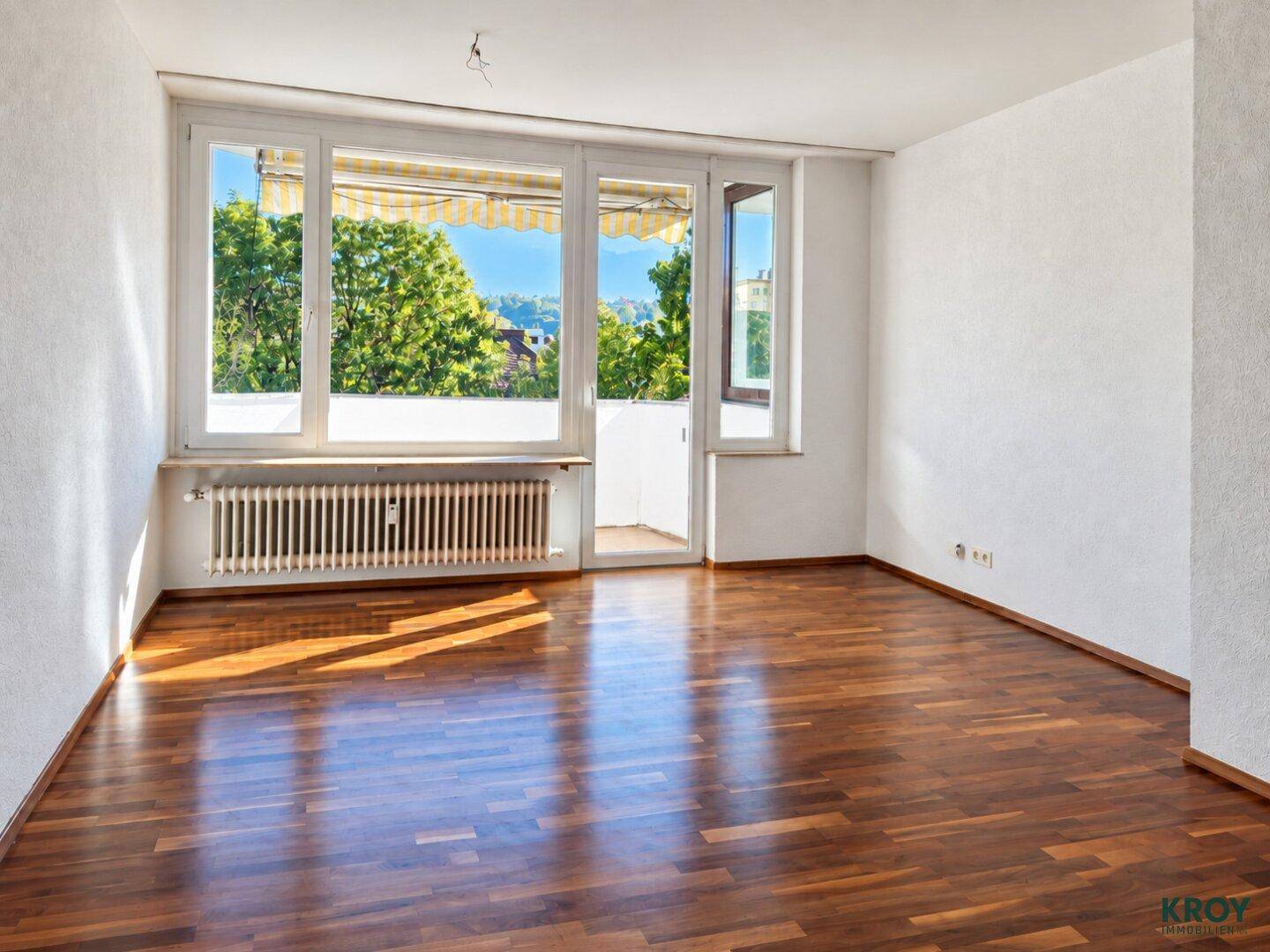 Helles Wohnzimmer mit glänzendem Parkettboden und Zugang zu einem sonnigen Balkon.