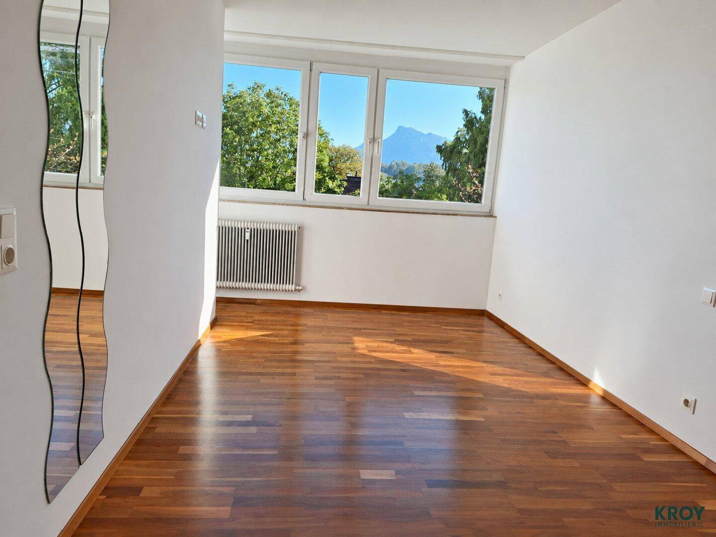 Geräumiges Schlafzimmer mit Parkettboden, großen Fenstern und einem dekorativen Spiegel.