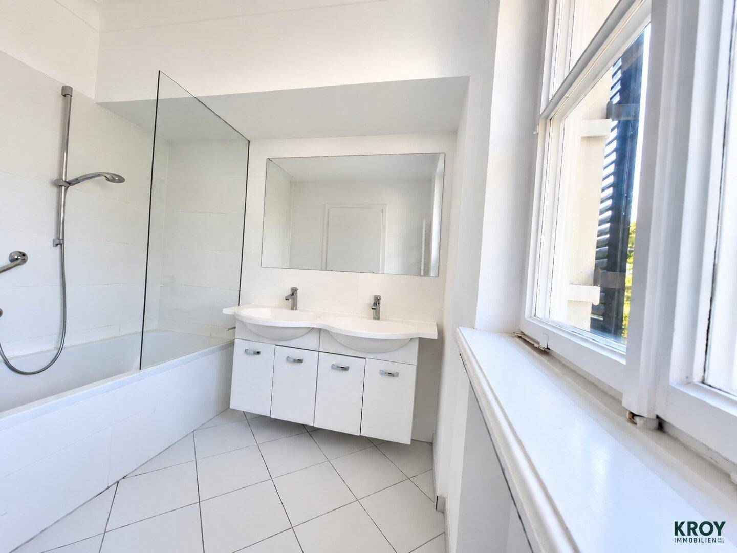 Modernes Badezimmer mit Doppelwaschbecken, Badewanne mit Duschabtrennung und Fenster.