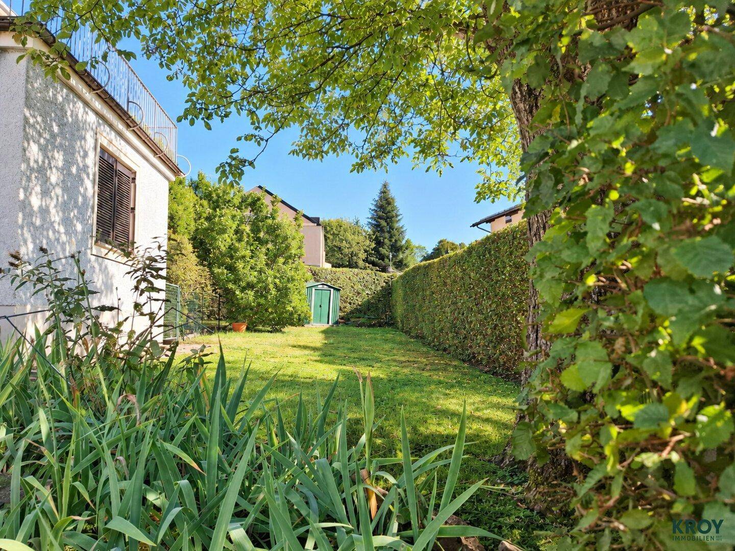 Gepflegter Garten mit Rasenfläche, hohen Hecken und einem kleinen Geräteschuppen.