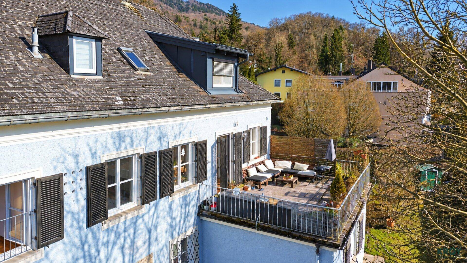 Hausfassade mit großer, möblierter Terrasse und Blick auf die umliegende grüne Hügellandschaft.