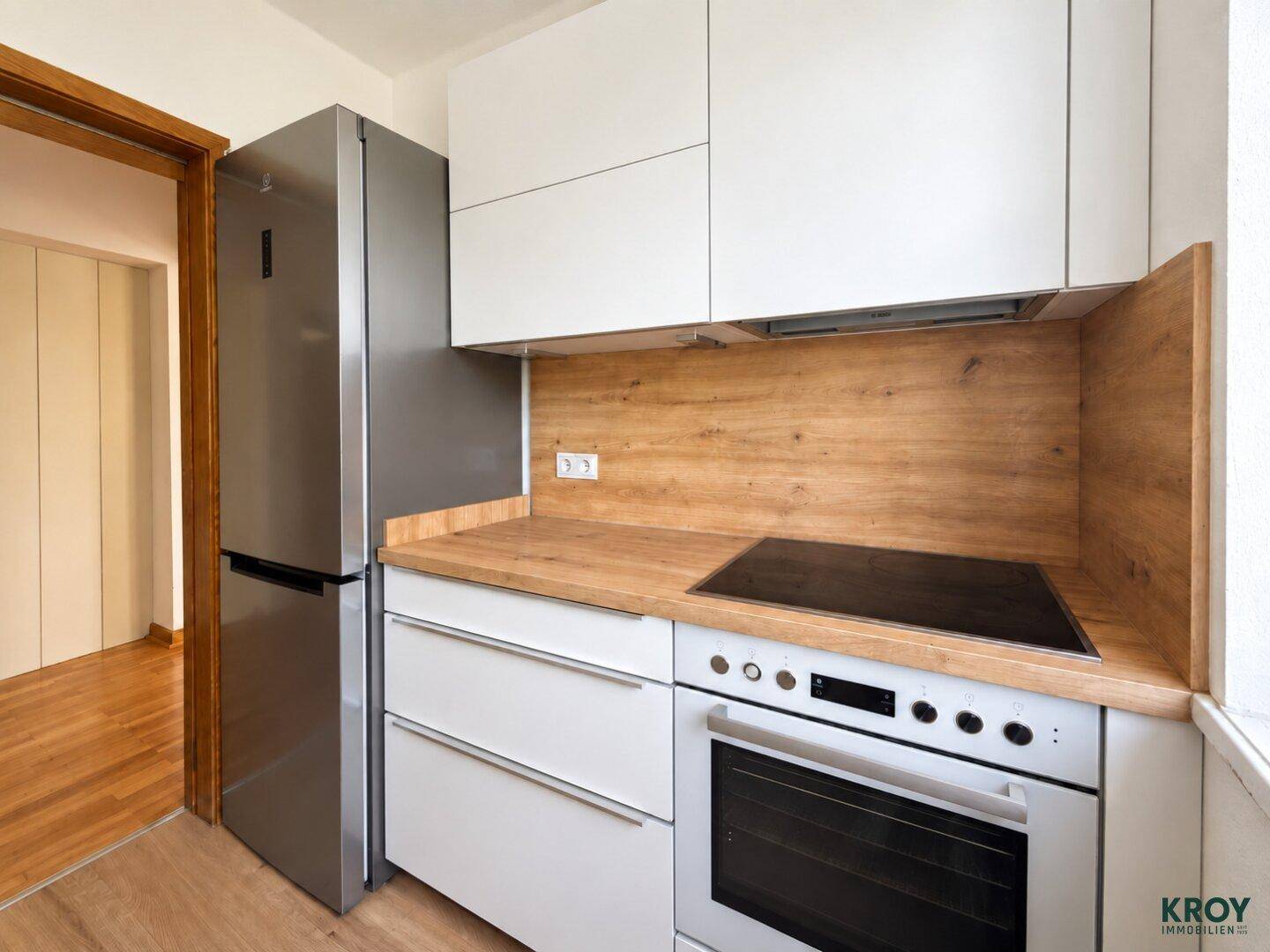 Funktionale Küche mit weißen Fronten, Holz-Arbeitsplatte, Induktionskochfeld und Kühlschrank.
