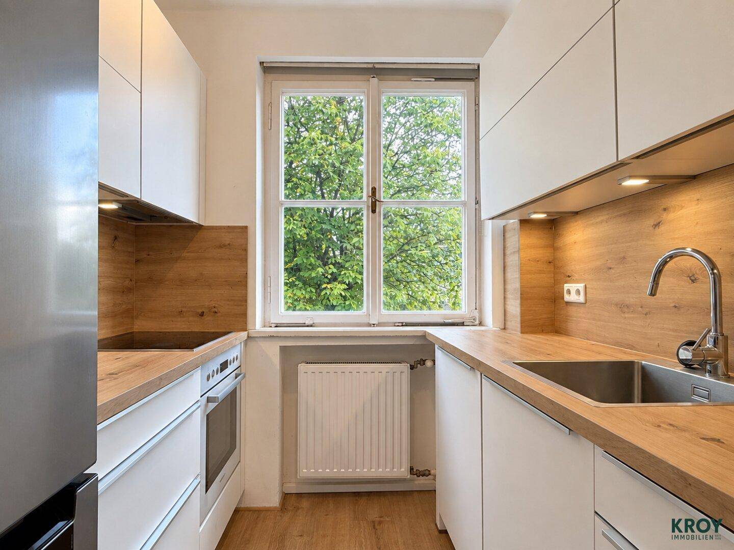 Moderne Küche mit weißen Schränken, Holz-Arbeitsplatten und Fenster mit Blick ins Grüne.