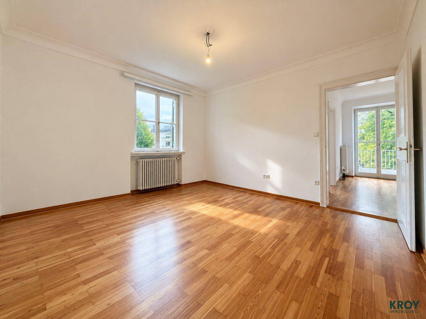 Helles Zimmer mit Parkettboden, weiß gestrichenen Wänden und Fenster mit Blick ins Grüne.