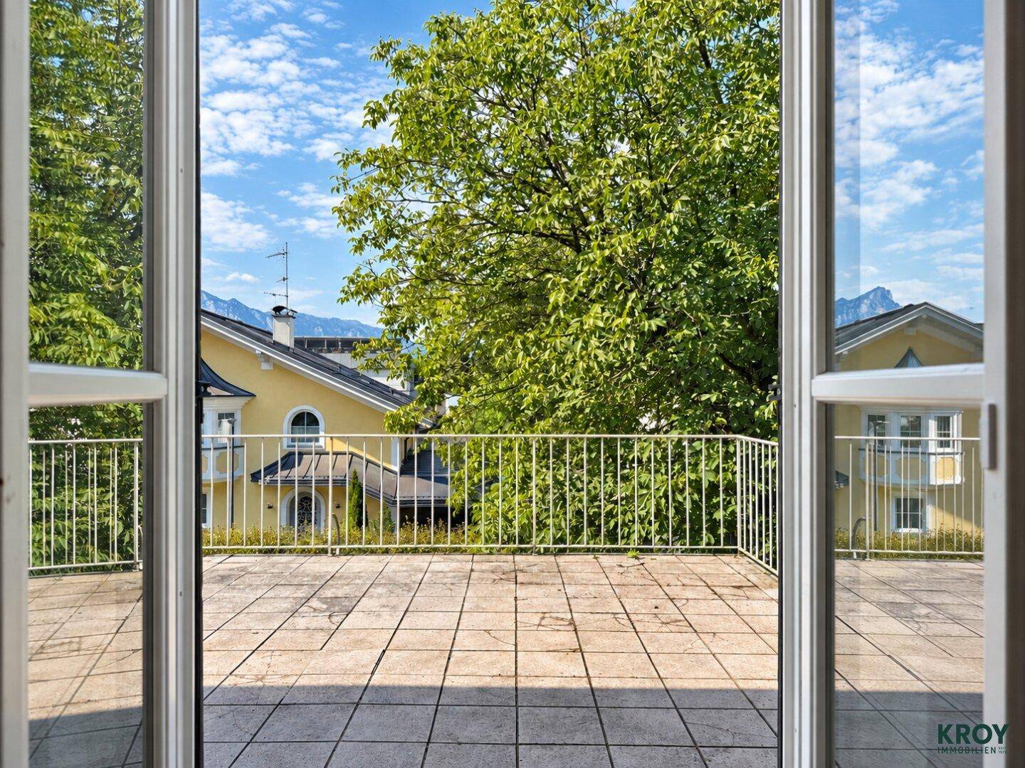 Große geflieste Terrasse mit Metallgeländer und Blick auf Bäume und Berge im Hintergrund.