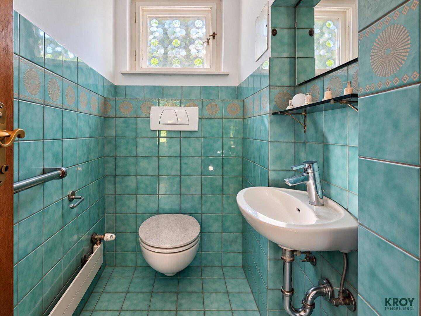 Kleines Badezimmer mit türkisfarbenen Fliesen, wandhängendem WC und Waschbecken.
