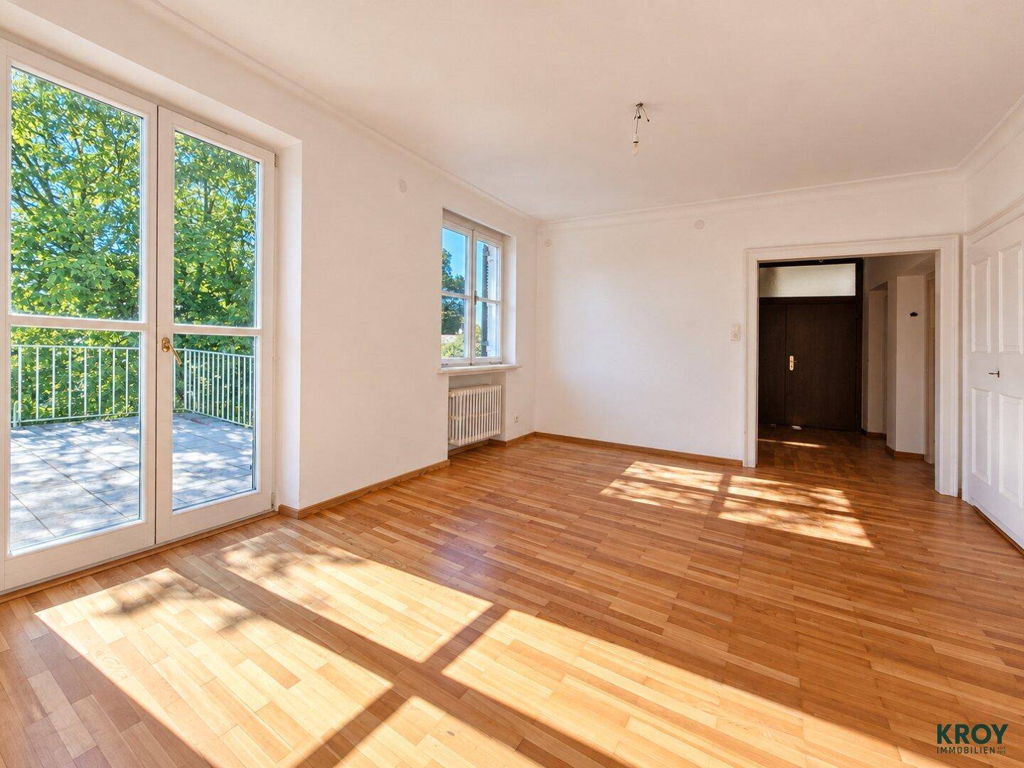 Geräumiges Zimmer mit Parkettboden, Zugang zur Terrasse und viel Tageslicht durch große Fenster.