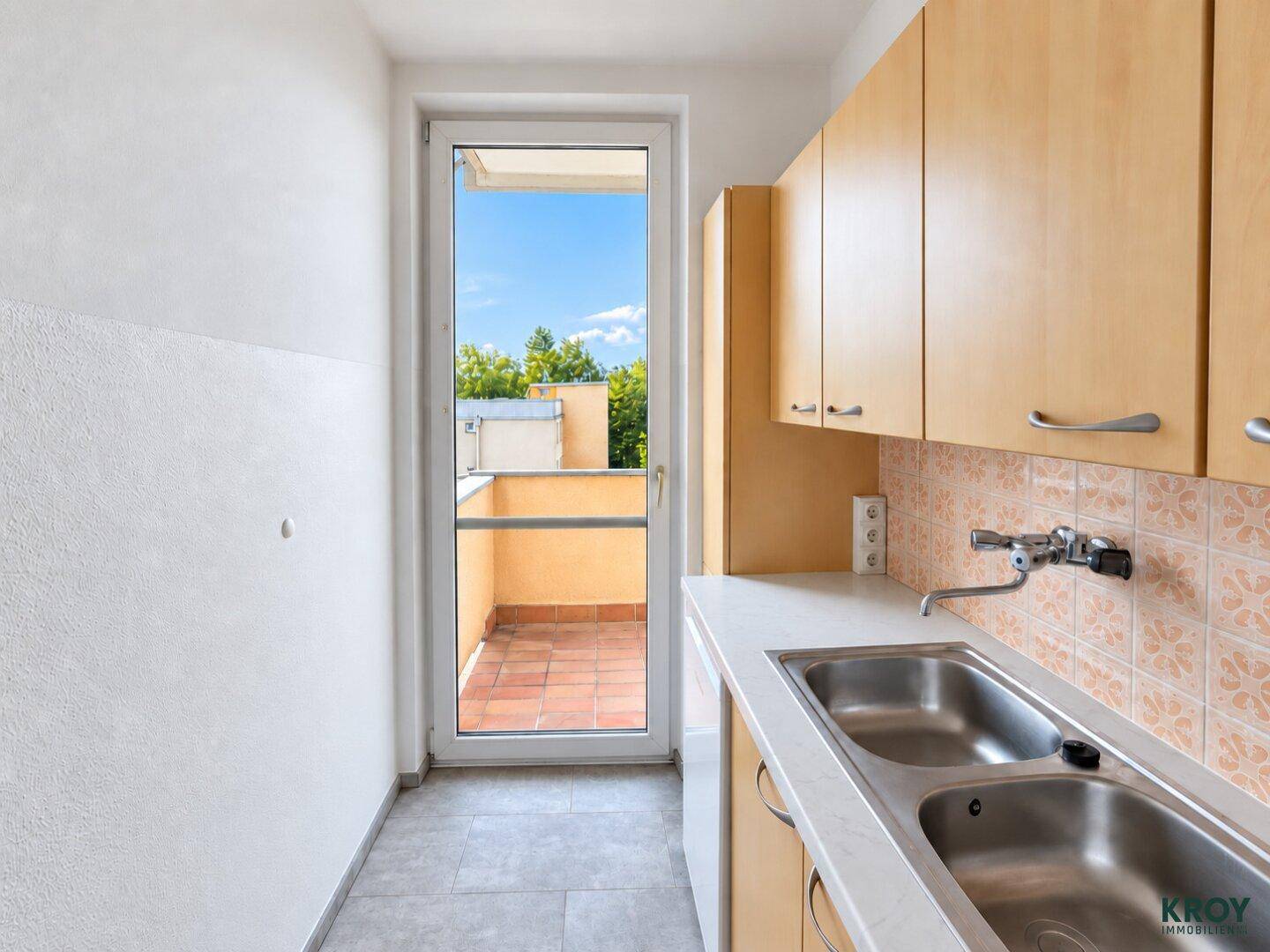 Kleine Küche mit Holzschränken, Doppelspüle und Zugang zu einem Balkon.