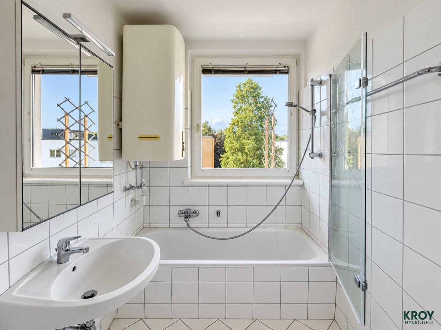 Helles Badezimmer mit Badewanne, Dusche und Fenster, komplett gefliest.